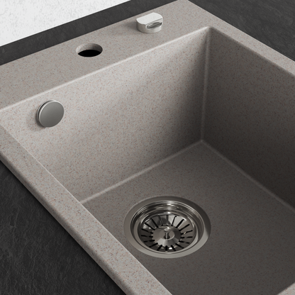 A single-basin drop-in kitchen sink made of speckled beige beach sand, stone or composite material, shown installed on a dark countertop with a matching faucet and drain visible.
